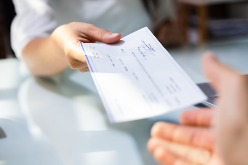 Image of a hand outstretched with a bank check in it and another hand reaching for the check.